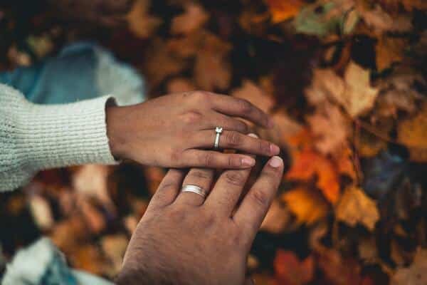 Dos manos tacándose, cada una lleva un anillo de plata. Debajo hojas de árboles secas en pleno otoño.