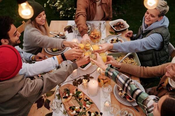 Amigos brindando en una mesa con comida, aperitivos, postres y bebidas. 