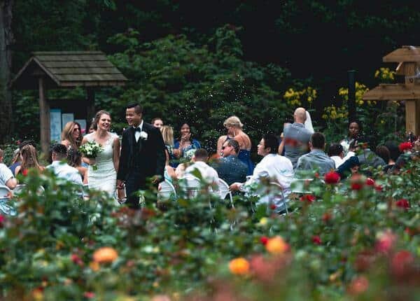 Pocas personas celebrando un matrimonio en una pequeño jardín lleno de flores amarillas, rojas y rosas. 
