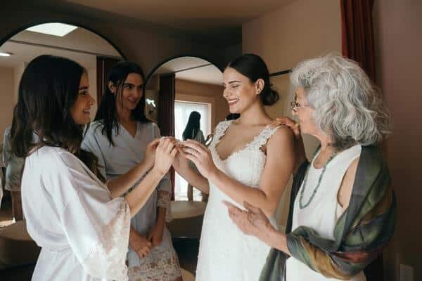 Mujeres alrededor de la novia, parecen ayudarla y apoyarla. De fondo un pequeño cuarto con espejos altos.