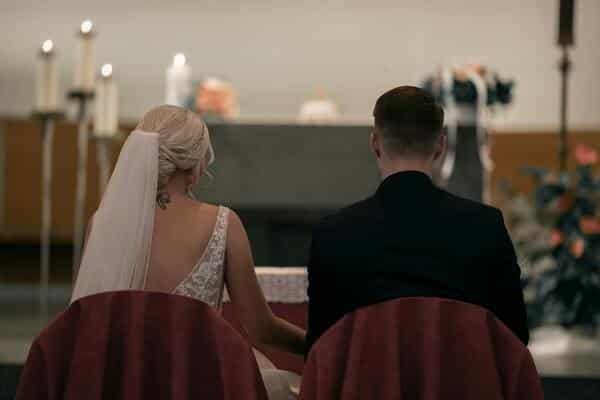 Dos novios sentados de espalda, viendo enfrente una iglesia. La novia lleva un vestido blanco y el novio un traje elegante y negro.