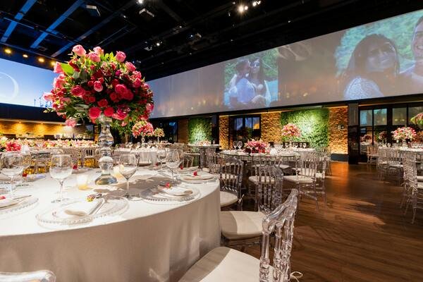 Salón de fiestas decorados para organizar boda en 6 meses. Mesas y sillas elegantes. Arriba de las mesas centros de mesa, copas, platos, servilletas y utensilios. 